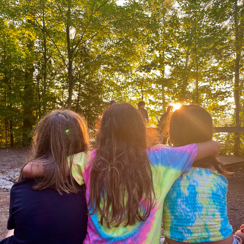 Three girls hugging in the forest at sunset