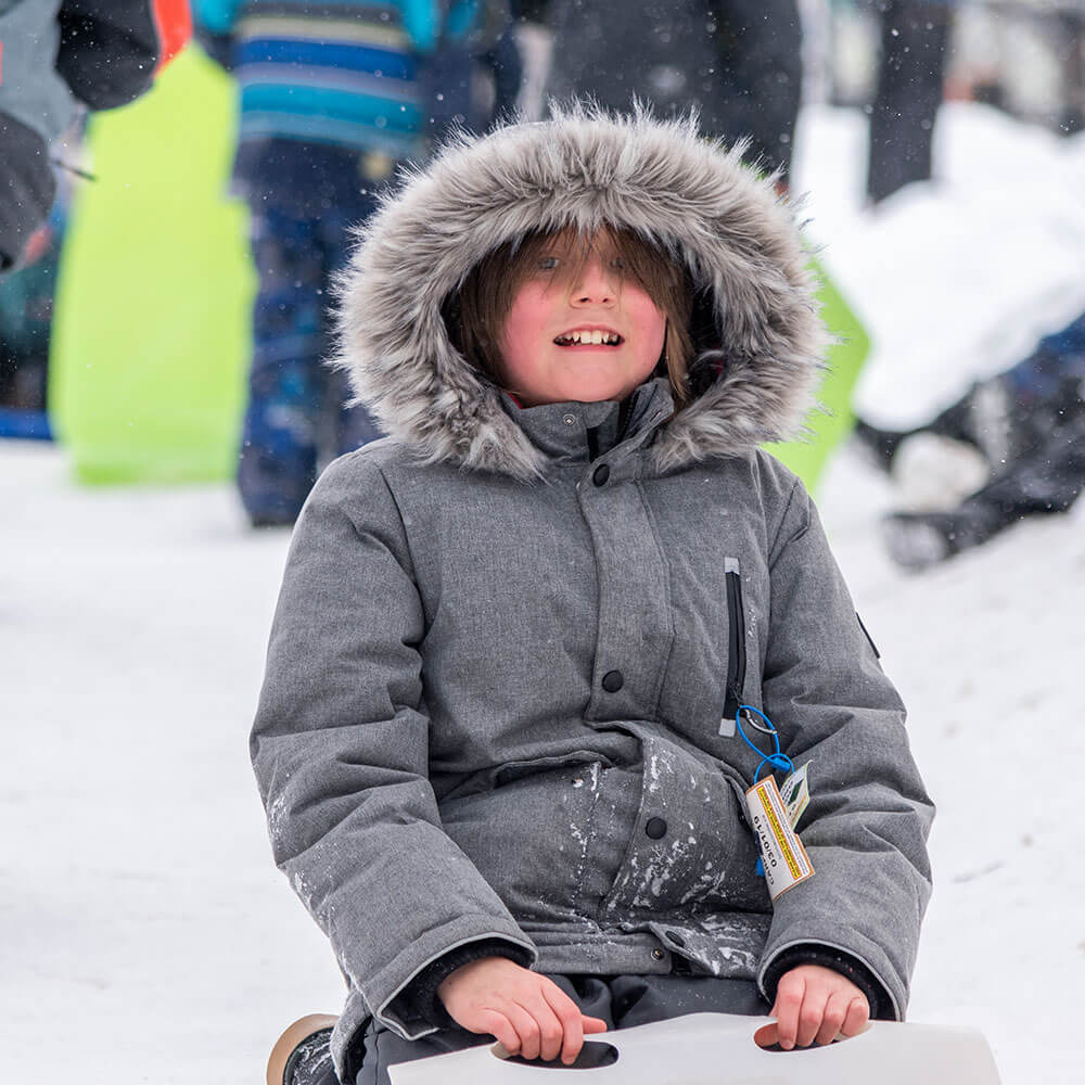 Kid smiling outside in winter coat with snow in background