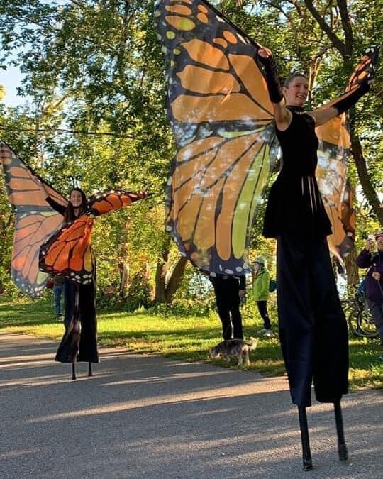 Women outside on stilts wearing butterfly wings