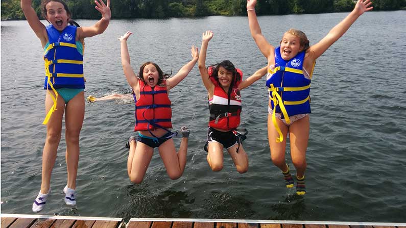 kids jumping into lake with lifejackets on
